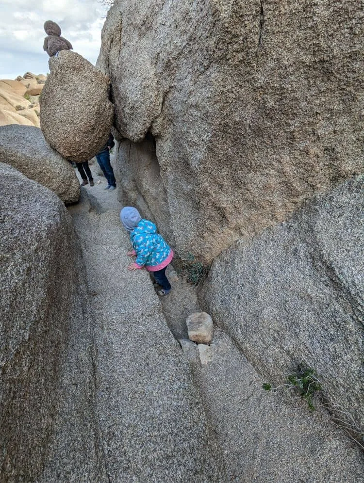 child climbing under a rock cave