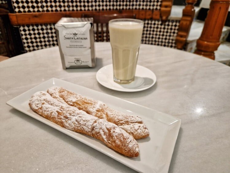 Horchata fresca servida en vaso alto junto a fartons espolvoreados con azúcar, sobre una mesa de mármol en la Horchatería Santa Catalina de Valencia.