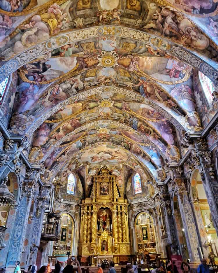 Interior de la Iglesia de San Nicolás en Valencia, mostrando sus impresionantes frescos que adornan las bóvedas y paredes, con detalles dorados en el altar mayor. Un patrimonio artístico que cautiva a visitantes y fieles por igual.