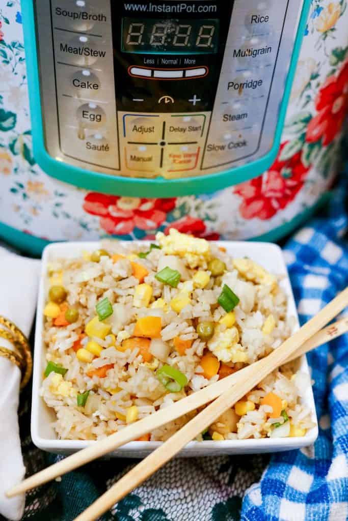 A bowl of easy fried rice with vegetables and scrambled eggs, garnished with green onions, placed in front of an Instant Pot. Chopsticks are laid across the bowl. One of the easiest Asian recipes!