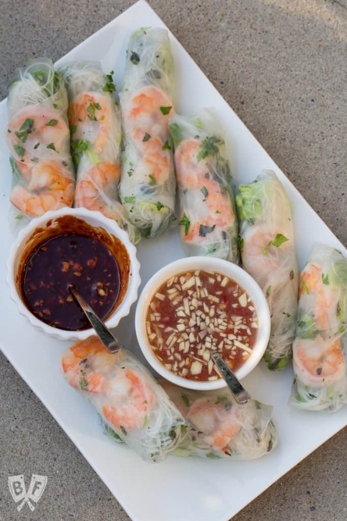 A platter of Vietnamese fresh spring rolls filled with shrimp, vermicelli noodles, and herbs, served with two dipping sauces in small bowls.