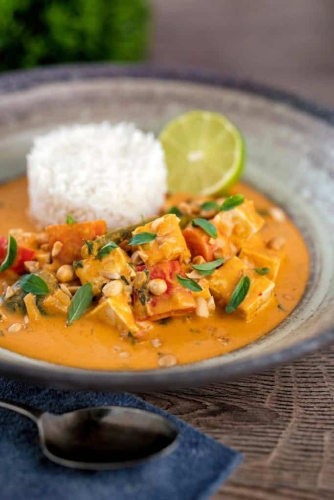 A bowl of Thai Panang curry with tofu and vegetables in a rich orange sauce, garnished with basil leaves and peanuts. One of the best Asian recipes.